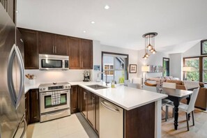 A modern kitchen with stainless steel appliances, a large island, and a dining area with a view.
