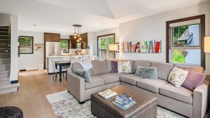 A modern living room with a sectional sofa, a coffee table, and a dining area with a kitchen in the background.