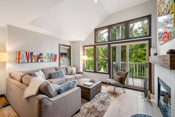 A spacious living room with a large window, a fireplace, and a modern sofa set.
