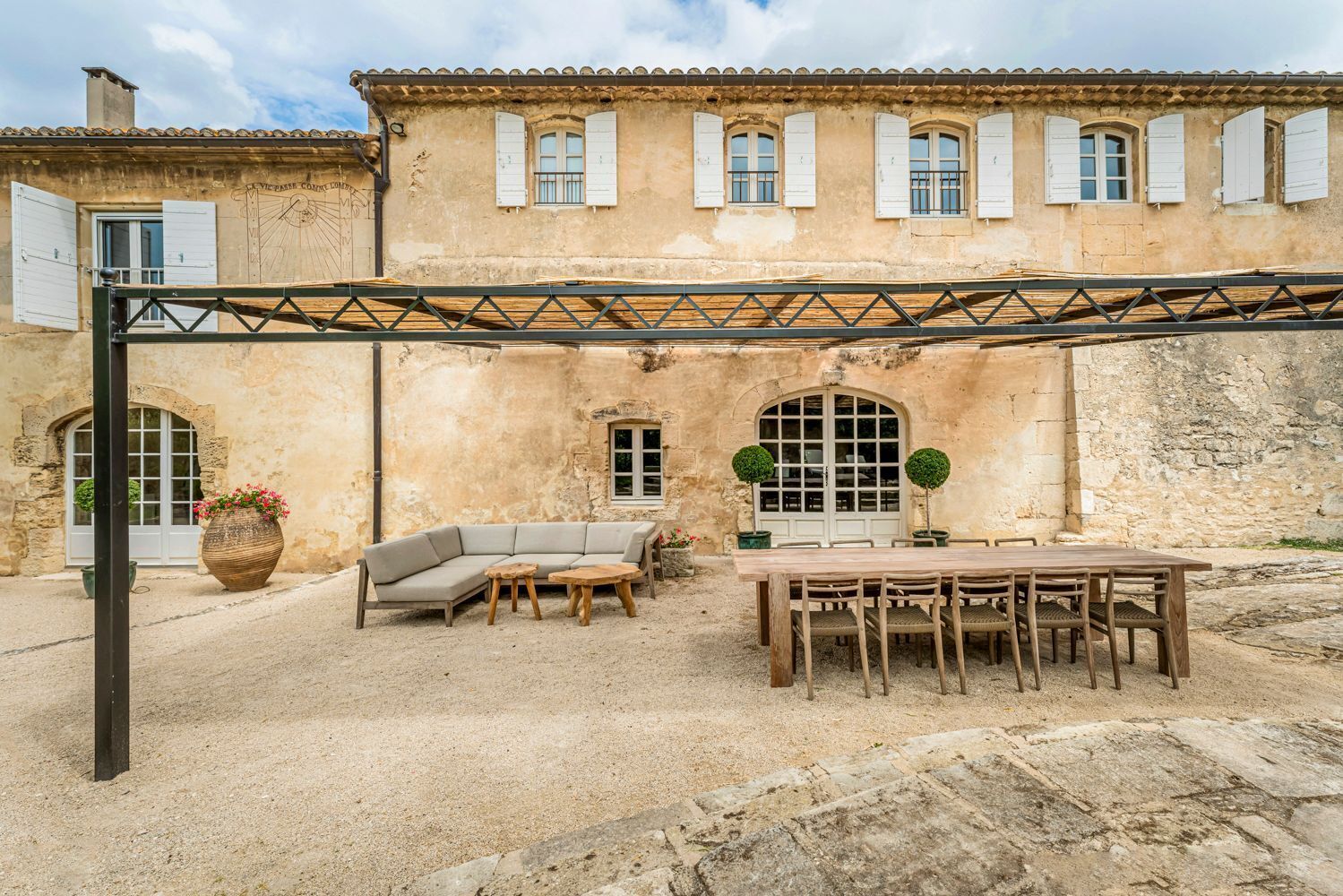 A courtyard with a wooden table and chairs, a sofa, and a large planter with flowers.