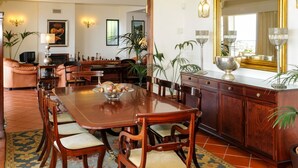 Een eetgedeelte met een houten tafel, stoelen en een decoratieve schaal. Achtergrond is een bank en een open haard.