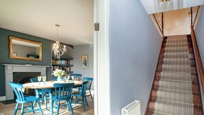 A dining area with a fireplace, a chandelier, and a staircase with a striped carpet. - UK45542-The Farm House (Sampford Courtenay, Okehampton)