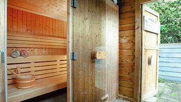Eine Holzsauna mit Sitzbank und Eimer, einer Glastür sowie einem Schild, das Schwimmbadnutzung verbietet.