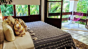 A bedroom with a large bed, a view of lush greenery through arched windows, and a balcony with a chair. - Steps to Ocean Playacar Villa Private Pool hosts 25+ guest (Playa del Carmen)
