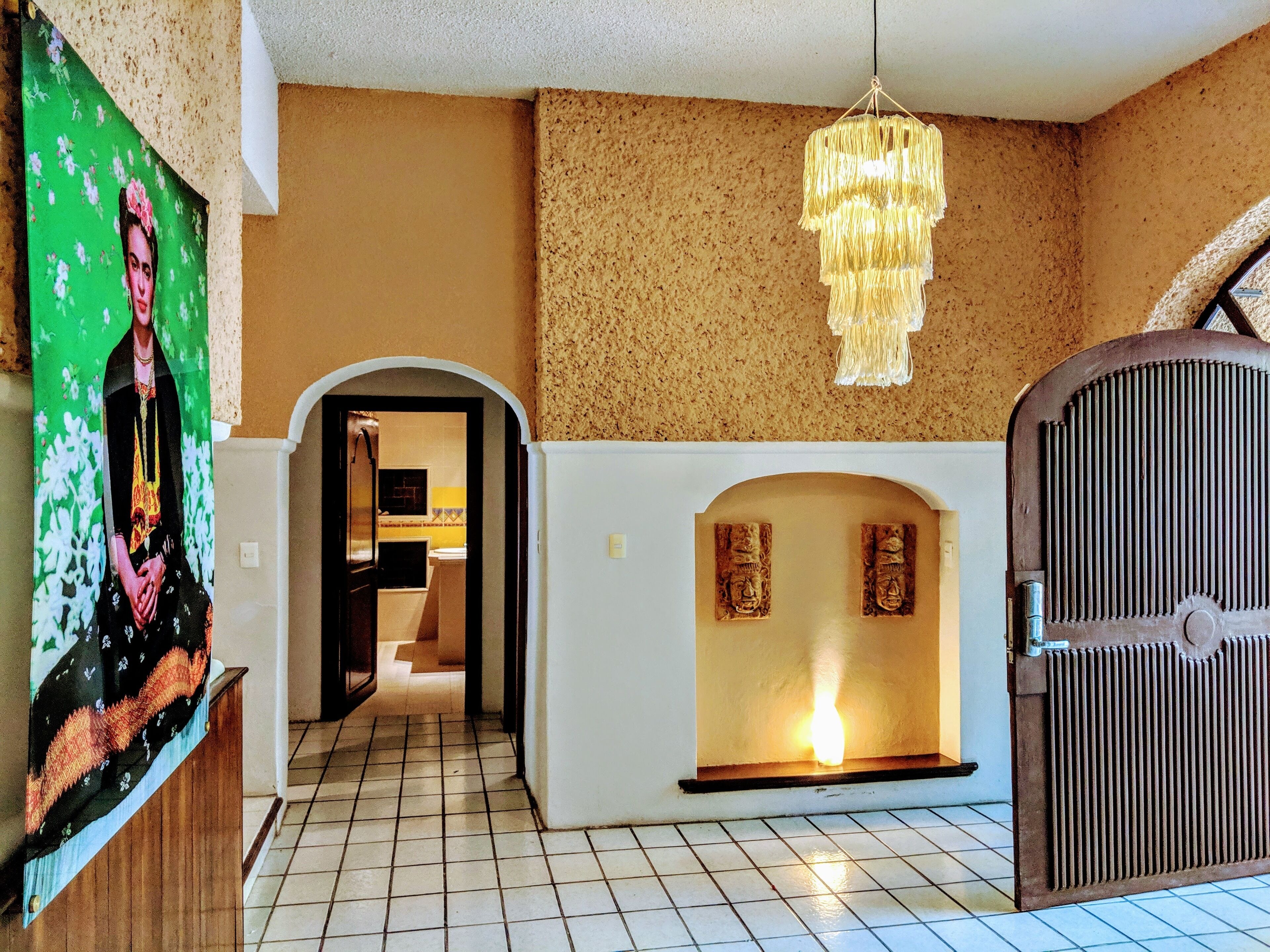 A hallway with a tiled floor, a green wall with a floral pattern, a white wall with a fireplace, and a large metal gate.
