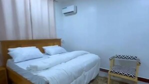 Un dormitorio con una cama, una silla y un equipo de aire acondicionado en la pared.
