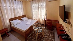 Un dormitorio con cama, escritorio, silla, televisor y aire acondicionado.