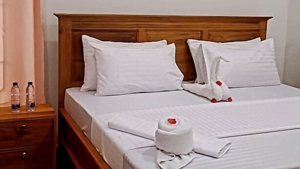 Una cama bien hecha con sábanas y almohadas blancas, un cabecero de madera y una mesita de noche con dos botellas.