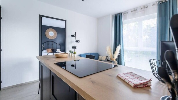 Een moderne keuken met een centraal eiland, een zwart aanrechtpaneel en een raam met blauwe gordijnen.