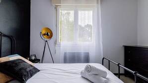 Een hotelkamer met een bed, een raam met gordijnen, een lamp en een dressoir.