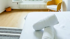 Una habitación con un ventanal grande, una silla amarilla y una cama con una toalla enrollada.