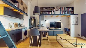 En kompakt bolig med tekøkken, spiseplads og et loftsrum med bogreoler.