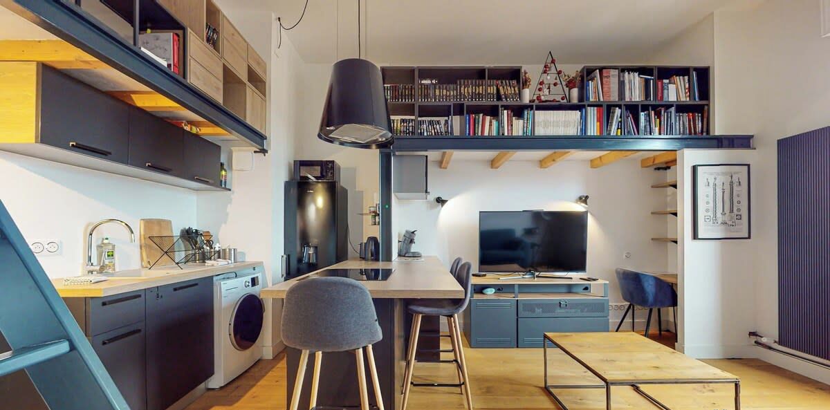 Een ruimtelijk ingedeelde leefruimte met een keuken, eethoek en een slaapverdieping met boekenkasten.