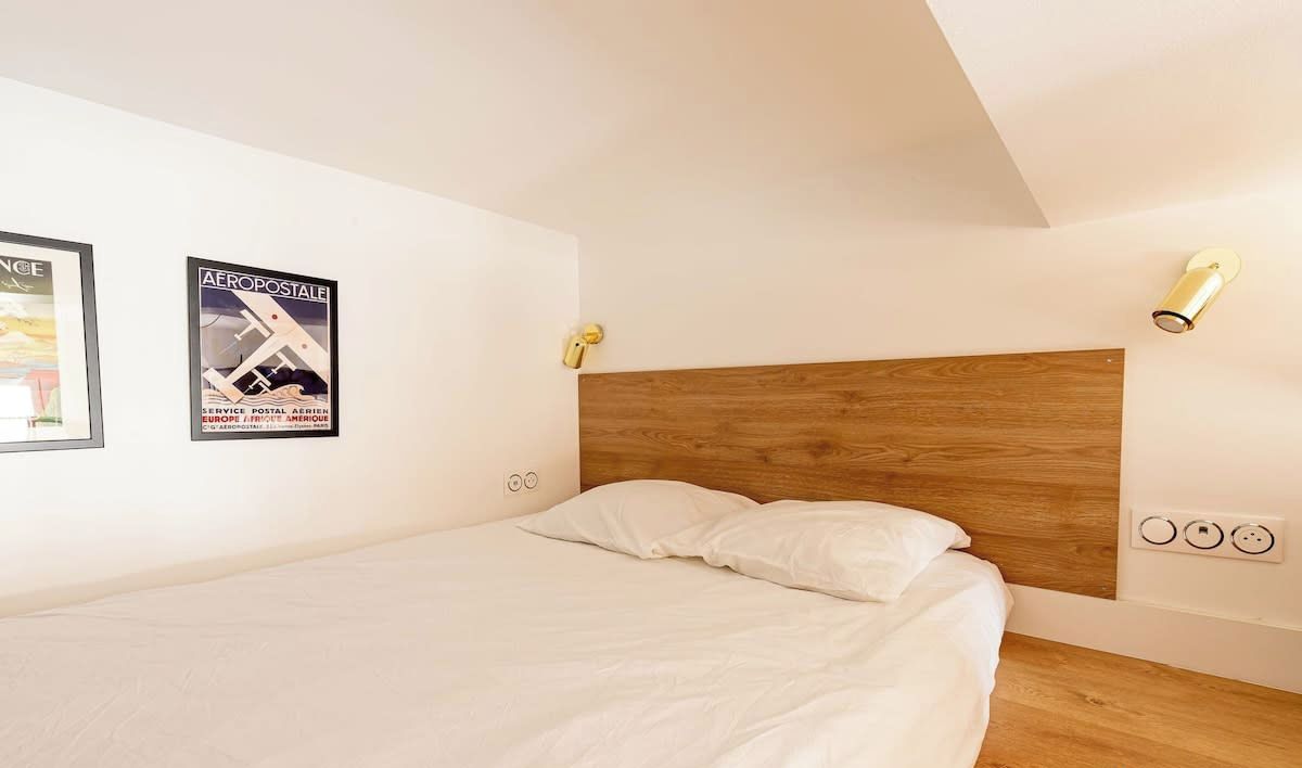 Une chambre à coucher avec une tête de lit en bois, une literie blanche et deux appliques murales.