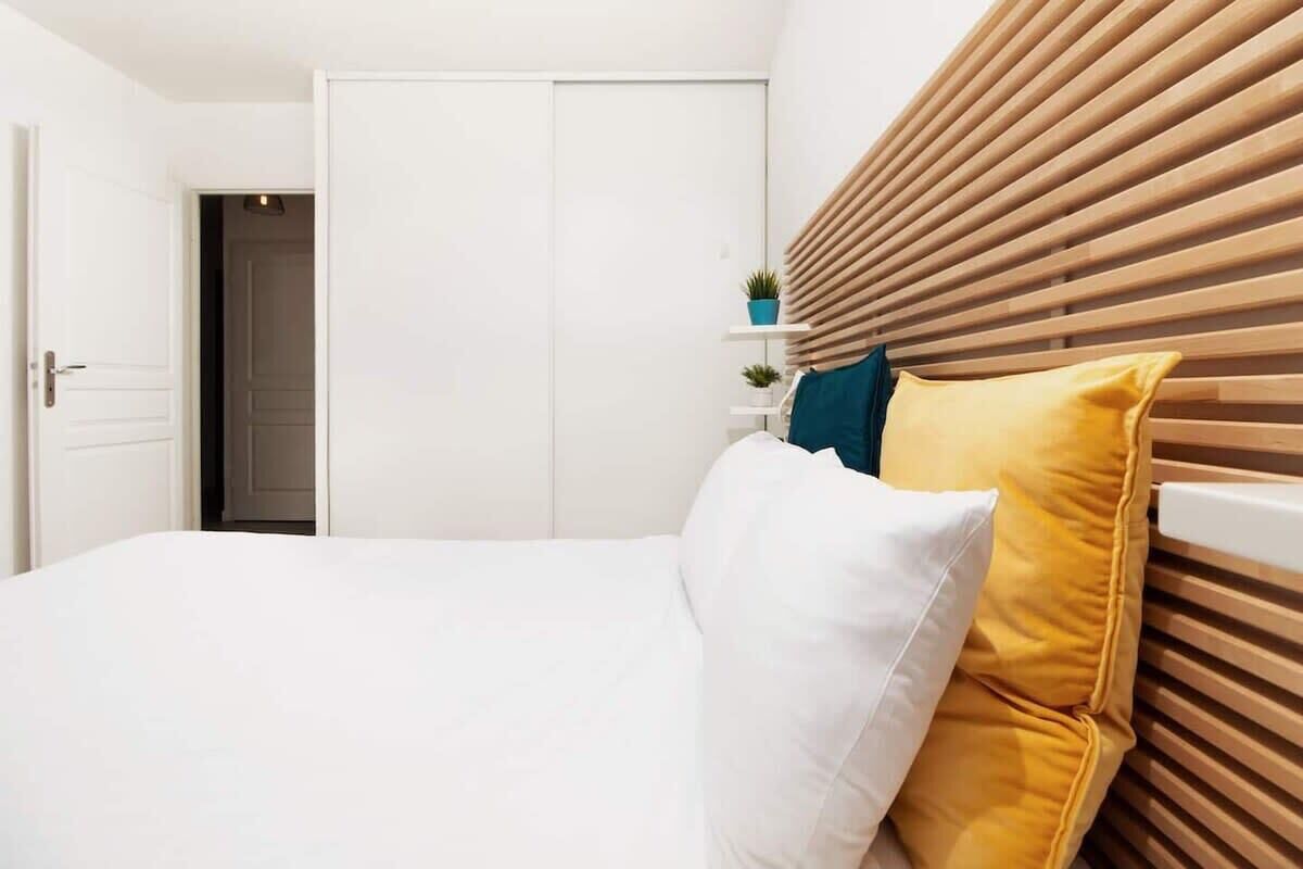 Une chambre à coucher avec un lit, des murs blancs, une tête de lit en bois et une porte fermée en arrière-plan.