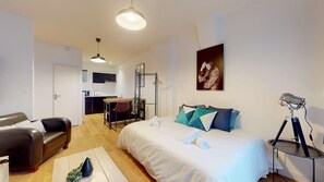 Ein modernes Hotelzimmer mit Bett, Schreibtisch, Stuhl, Sofa und einem kleinen Tisch mit Lampe.