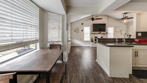 A modern kitchen with a central island, built-in appliances, and a dining area with a wooden table and bench. - Cute home with a Backyard pool! (San Antonio)