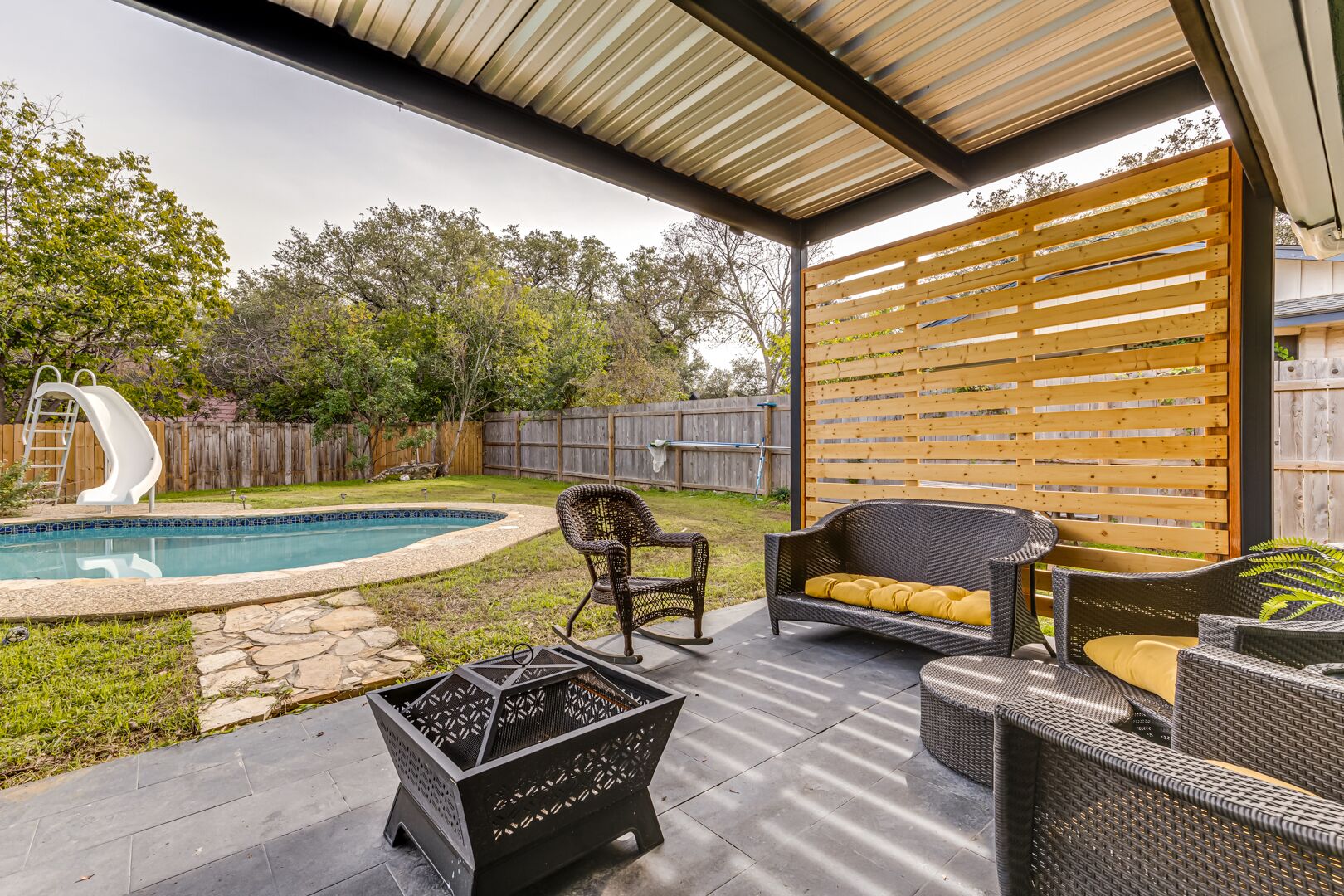 Ein überdachter Patio-Bereich mit Pool, Gartenmöbeln und einer Holz-Privatsphärenwand.