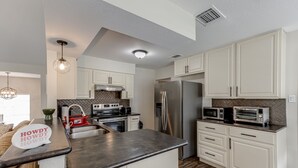 A modern kitchen with white cabinets, stainless steel appliances, and a herringbone-patterned backsplash. - Cute home with a Backyard pool! (San Antonio)
