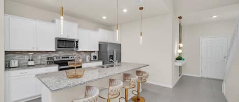 Une cuisine moderne avec des meubles blancs, un plan de travail en granit et un îlot central doté de tabourets de bar.