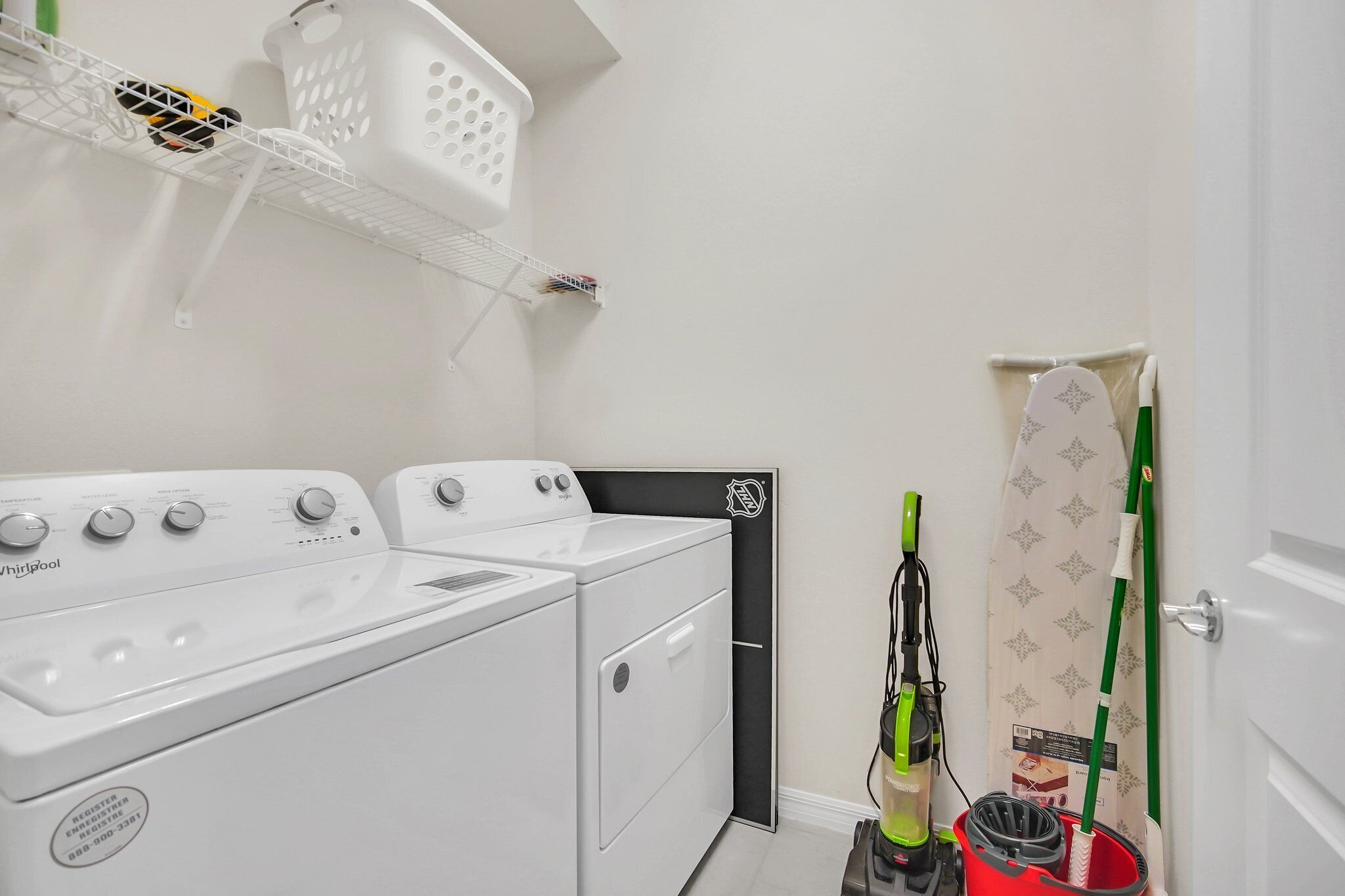 A laundry area with a front-loading washer and dryer, a drying rack, and a mop and bucket.