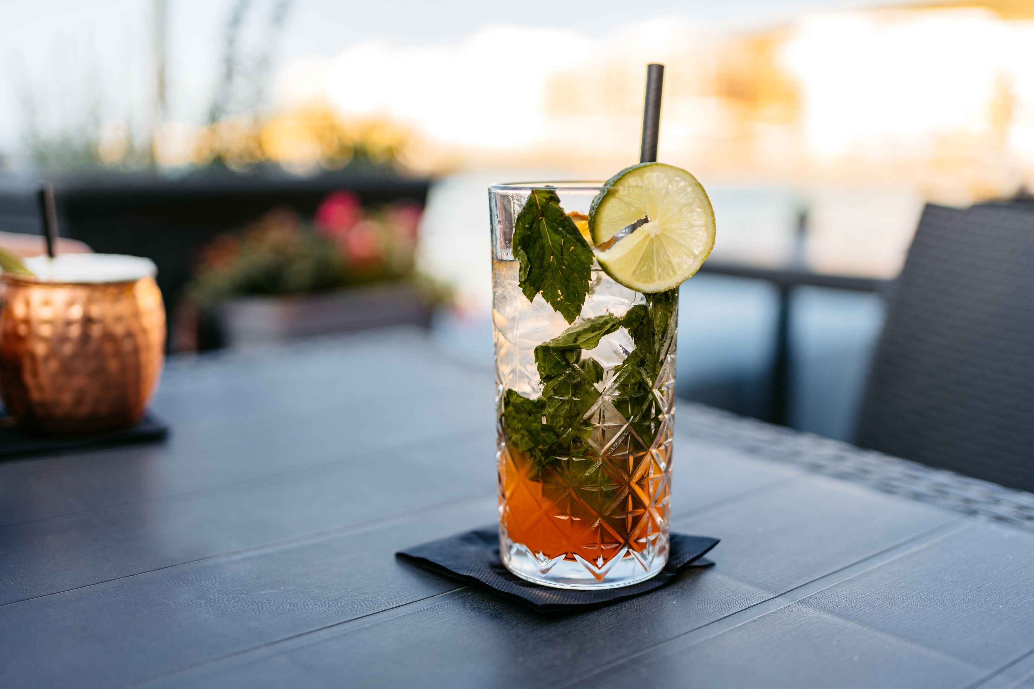 A glass of iced tea with mint leaves and a lime slice on a table with a napkin.