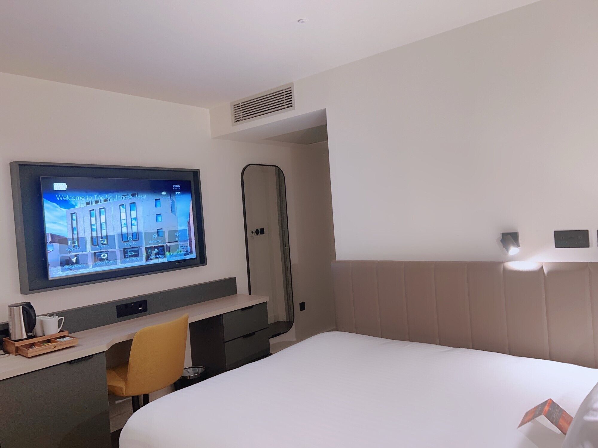A hotel room with a bed, a desk with a computer, a TV mounted on the wall, and a shower area.