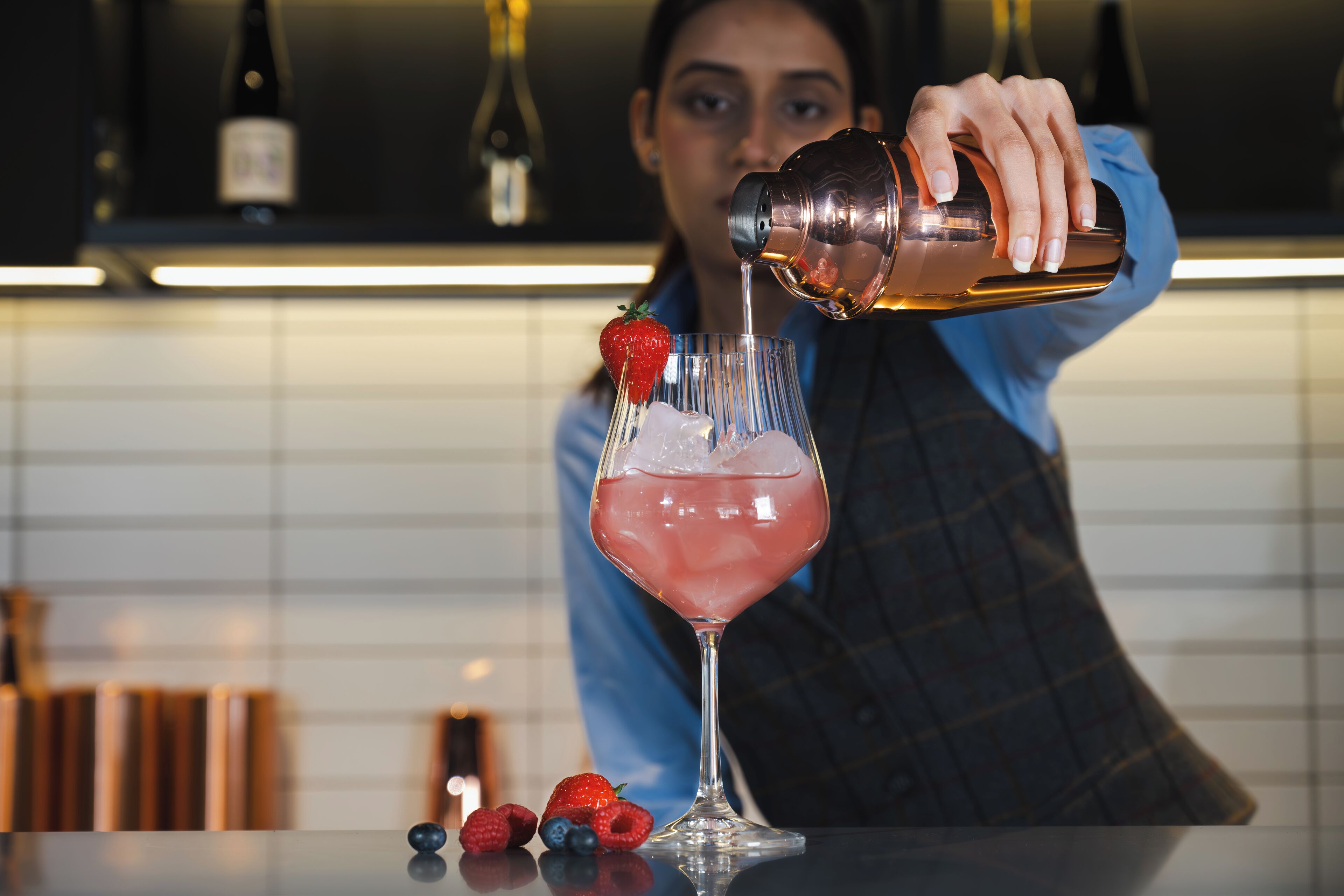 Un barman verse une boisson dans un verre, qui est décoré d’une fraise.