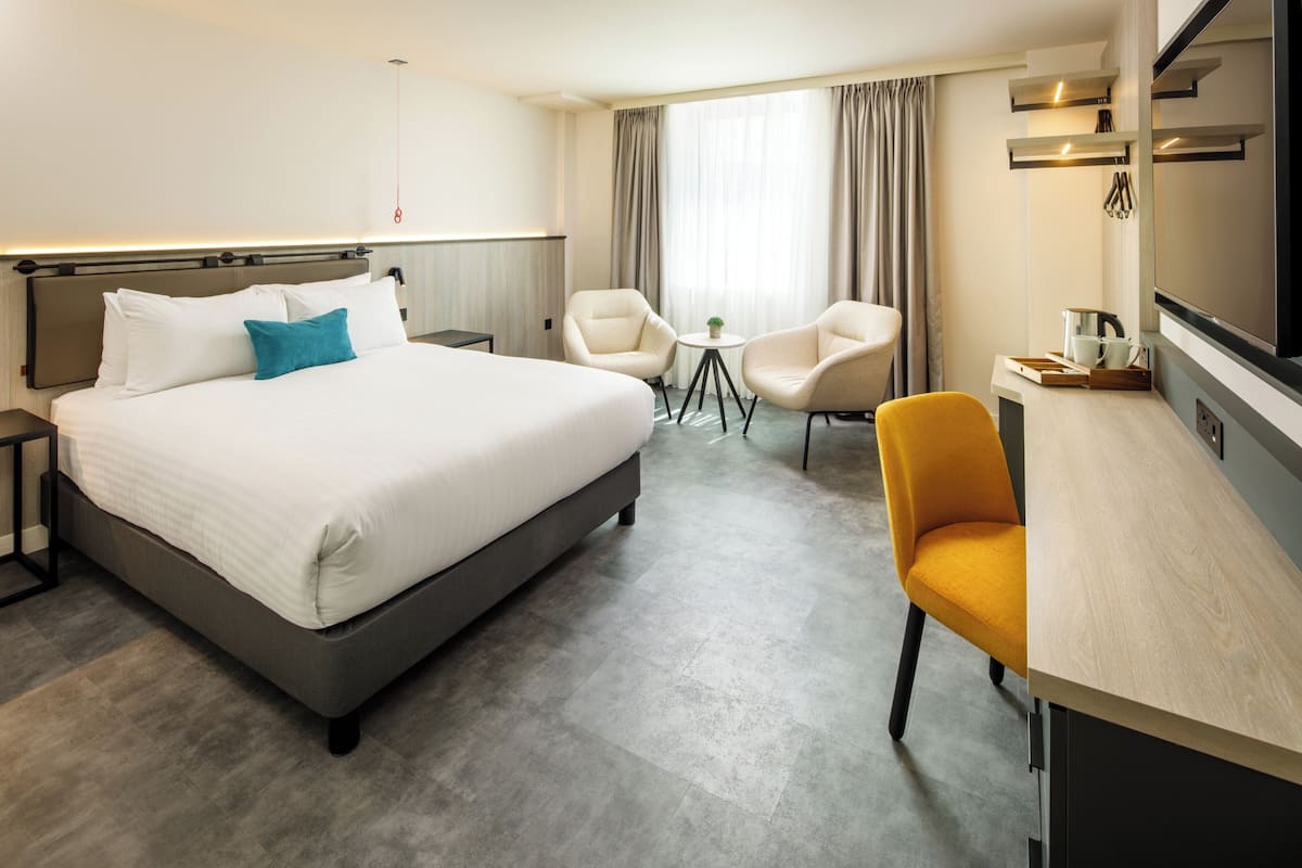 A hotel room with a large bed, two chairs, a small table, and a desk with a chair.