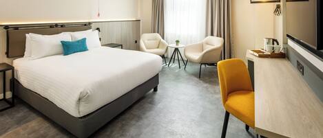 Ein Hotelzimmer mit einem großen Bett, zwei Sesseln, einem kleinen Tisch und einem Schreibtisch mit Stuhl.