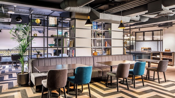 A modern lounge area with a sofa, chairs, a table, and a bookshelf. - Southgate Hotel London (London)