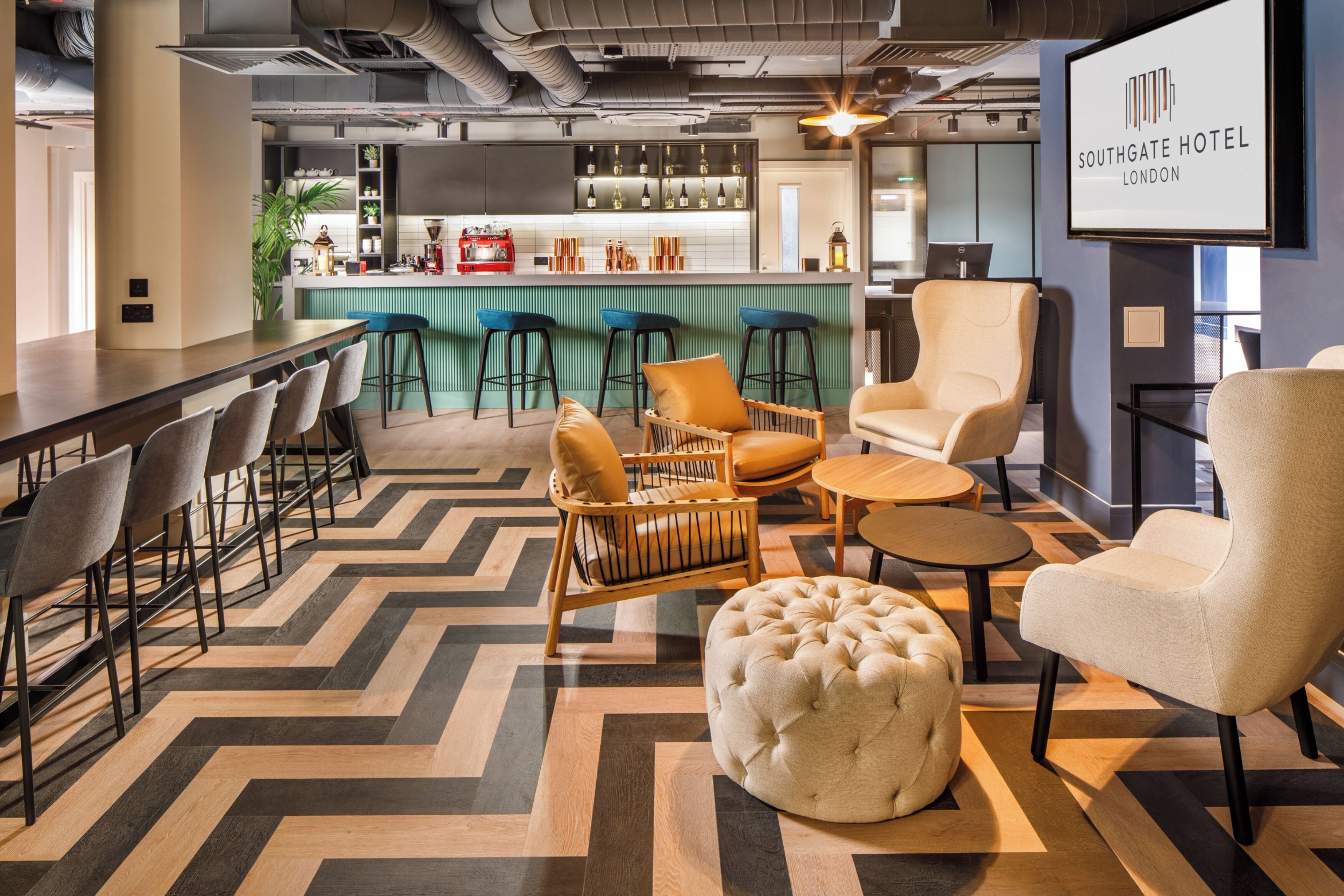 A modern hotel lobby with a bar area, seating arrangements, and a television displaying the hotel name.