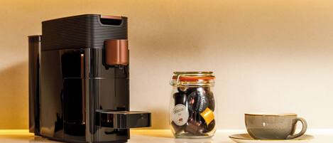 A coffee maker, a jar of coffee pods, and a cup on a countertop.