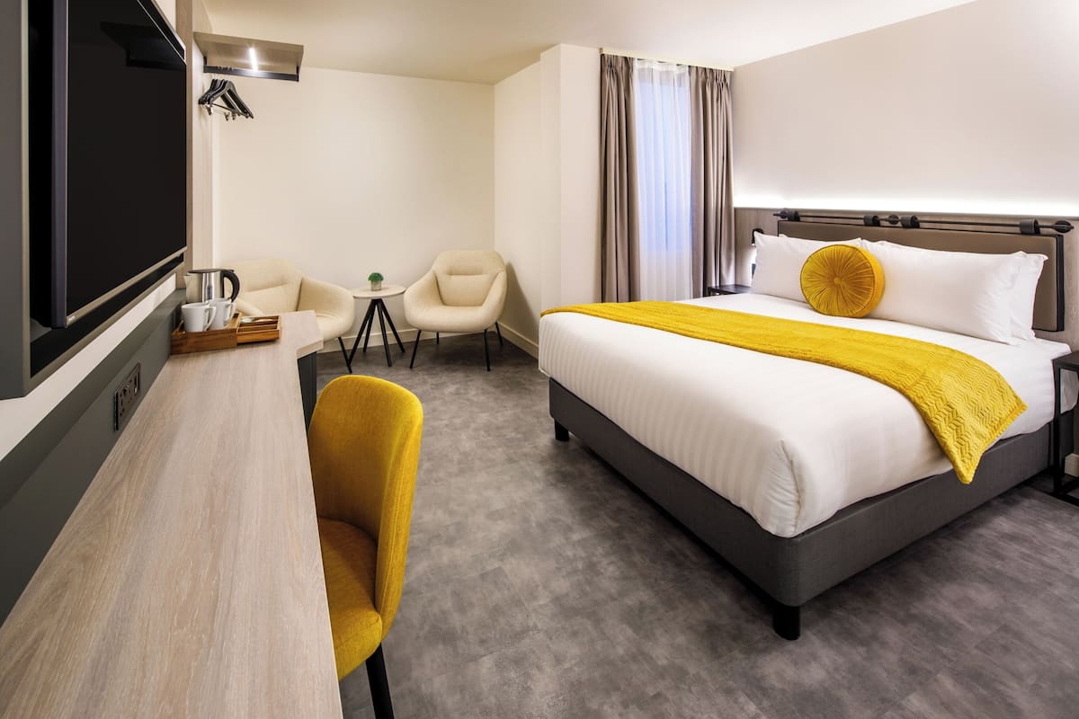 A hotel room with a bed, a desk, a chair, and a television.