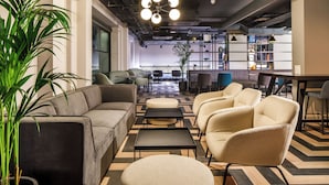 A modern lounge area with sofas, ottomans, and a coffee table. There are bookshelves and a potted plant. - Southgate Hotel London (London)