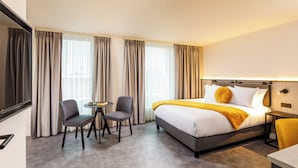 A hotel room with a bed, two chairs, a small table, and a TV. - Southgate Hotel London (London)