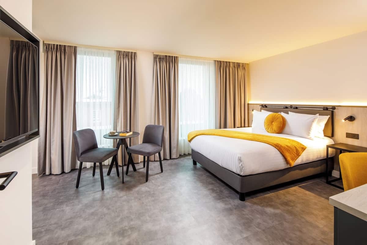 A hotel room with a bed, two chairs, a small table, and a TV.