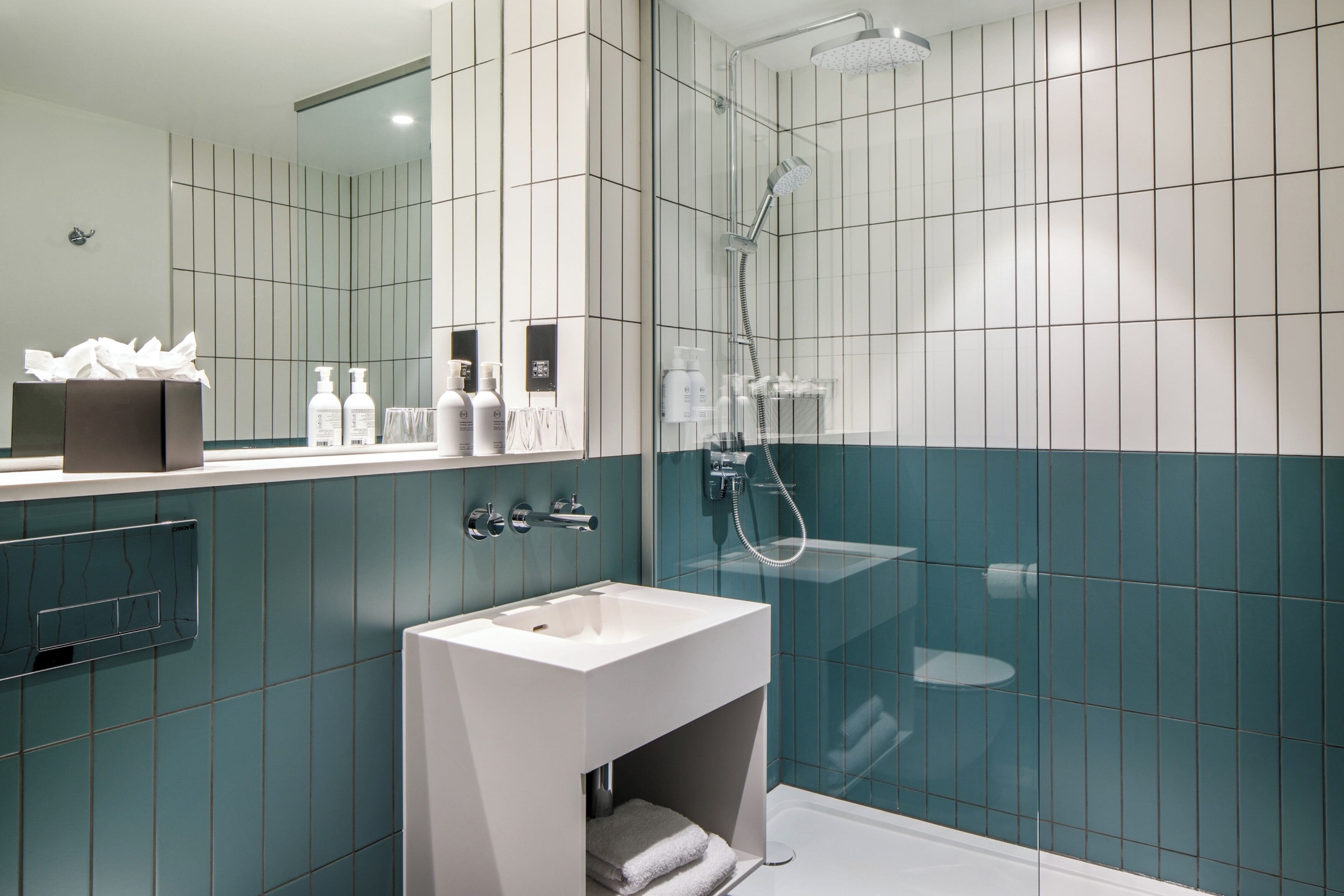 A modern bathroom with a white sink, a glass-enclosed shower, and teal tiles.