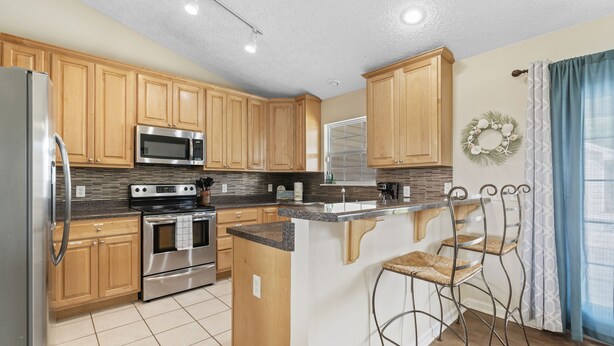 A kitchen with wooden cabinets, stainless steel appliances, a central island with bar stools, and a decorative wreath on the wall. - Michigan (Lynn Haven)
