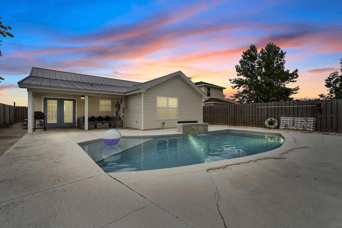 A residential backyard with a swimming pool, a wooden fence, and a house with a porch.