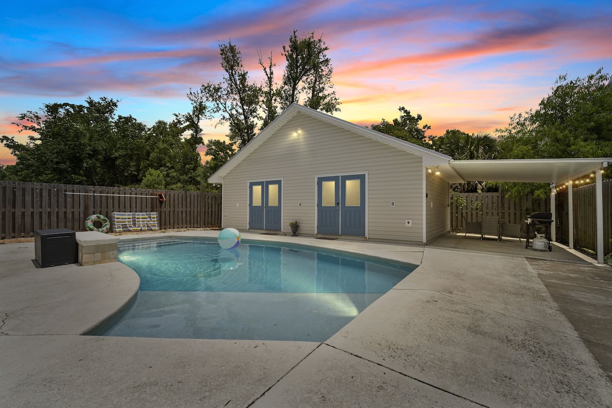 A backyard with a swimming pool, a covered patio, and a small house.
