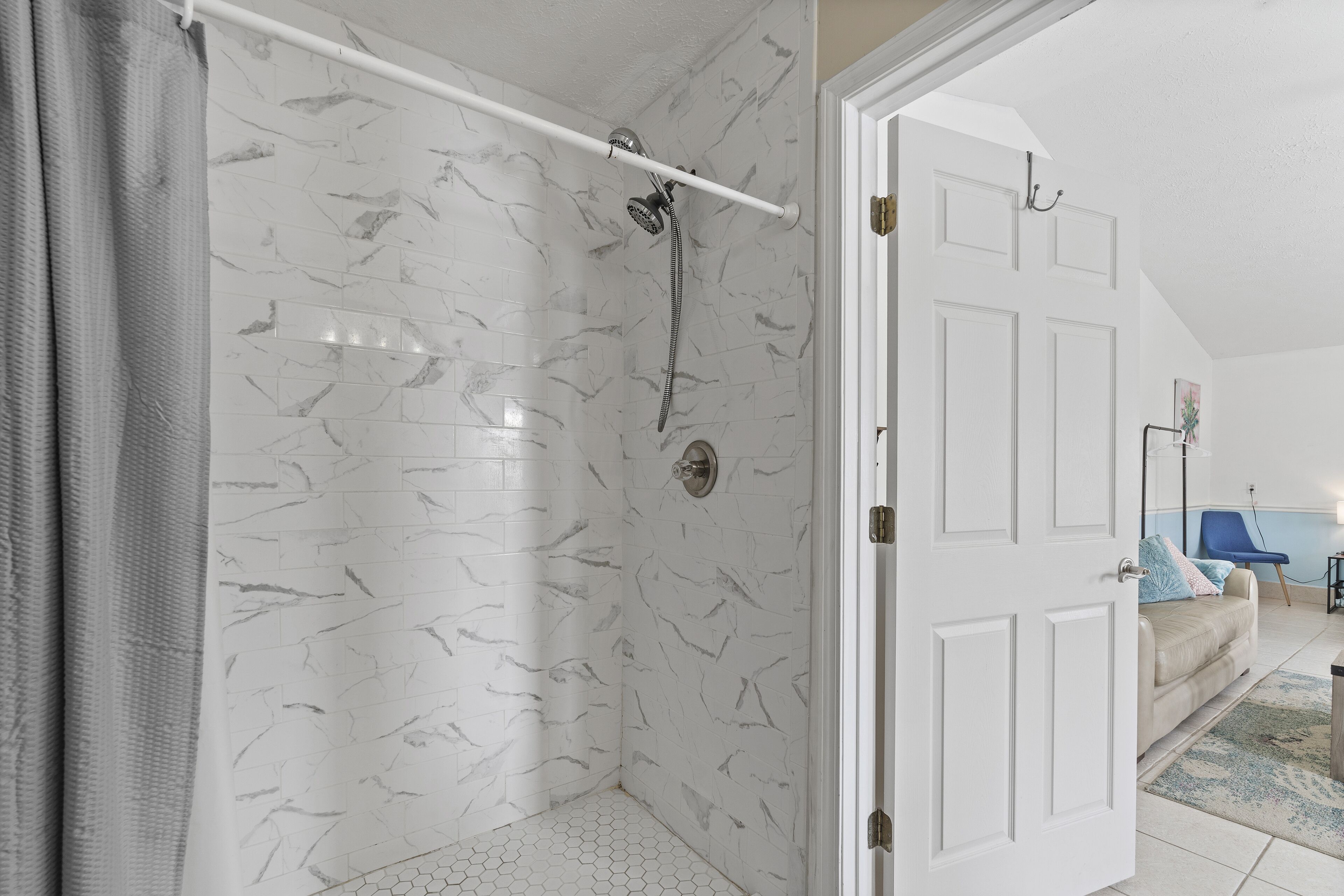A bathroom with a shower, white tiled walls, and a hexagonal floor pattern.