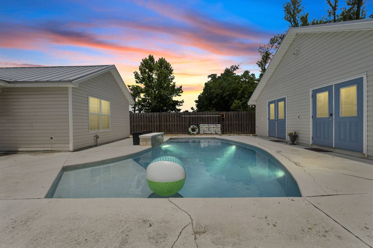 A swimming pool with a green and white ball, surrounded by two buildings with blue doors and windows, under a sunset sky.