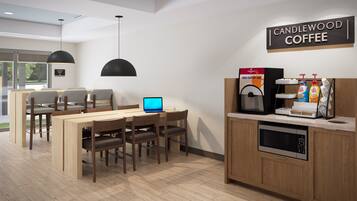Interior moderno de una cafetería con una computadora portátil sobre una mesa, una máquina de café y un letrero que dice 'CANDLEWOOD COFFEE'.