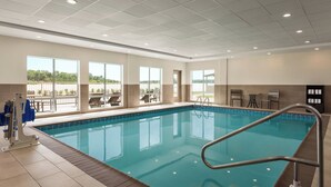 Piscina interna com vista ampla para o exterior, um posto de salva-vidas e área de estar com cadeiras e mesas.