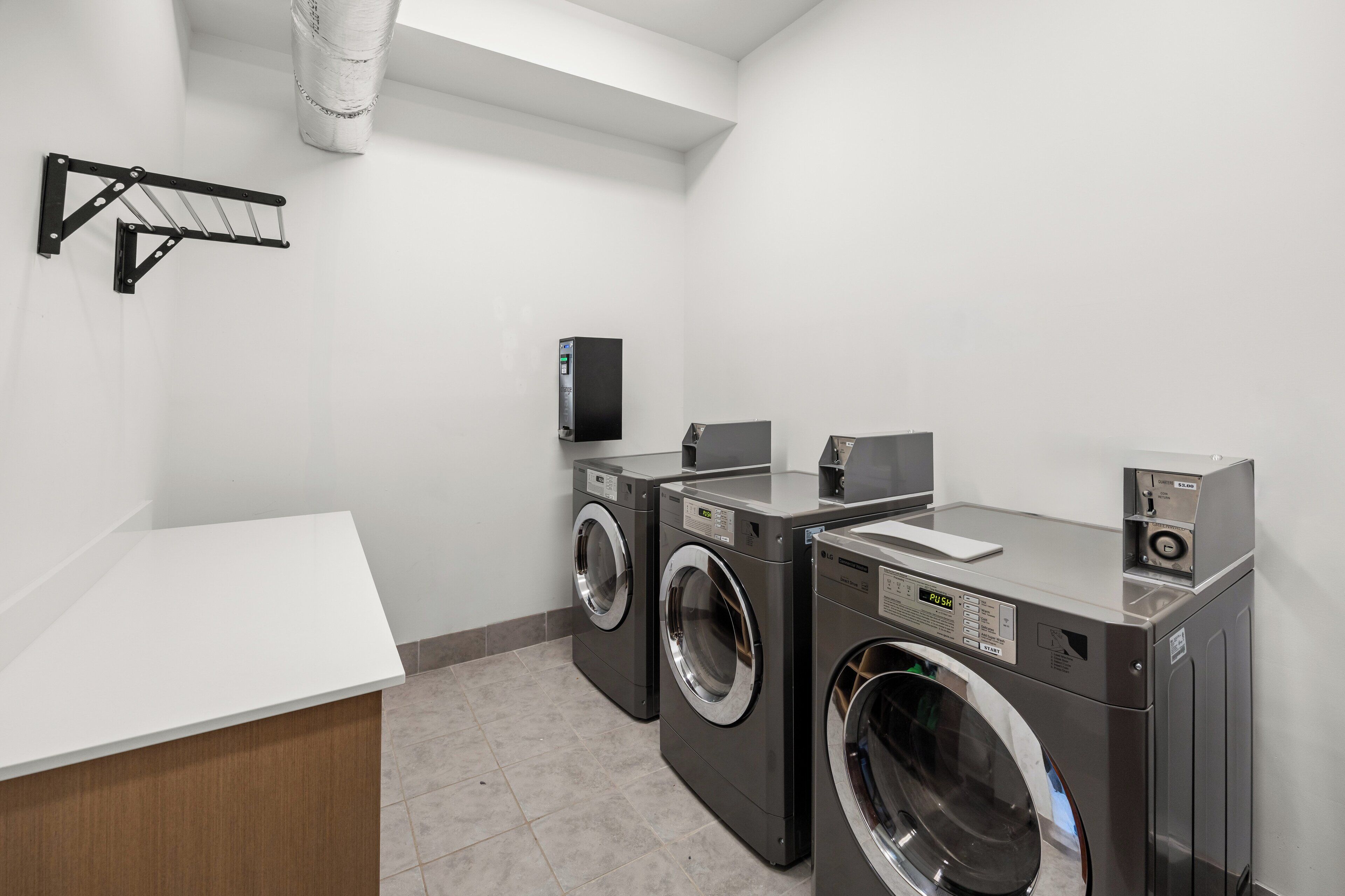 A laundry room with two front-loading washing machines, a dryer, and a wall-mounted drying rack.