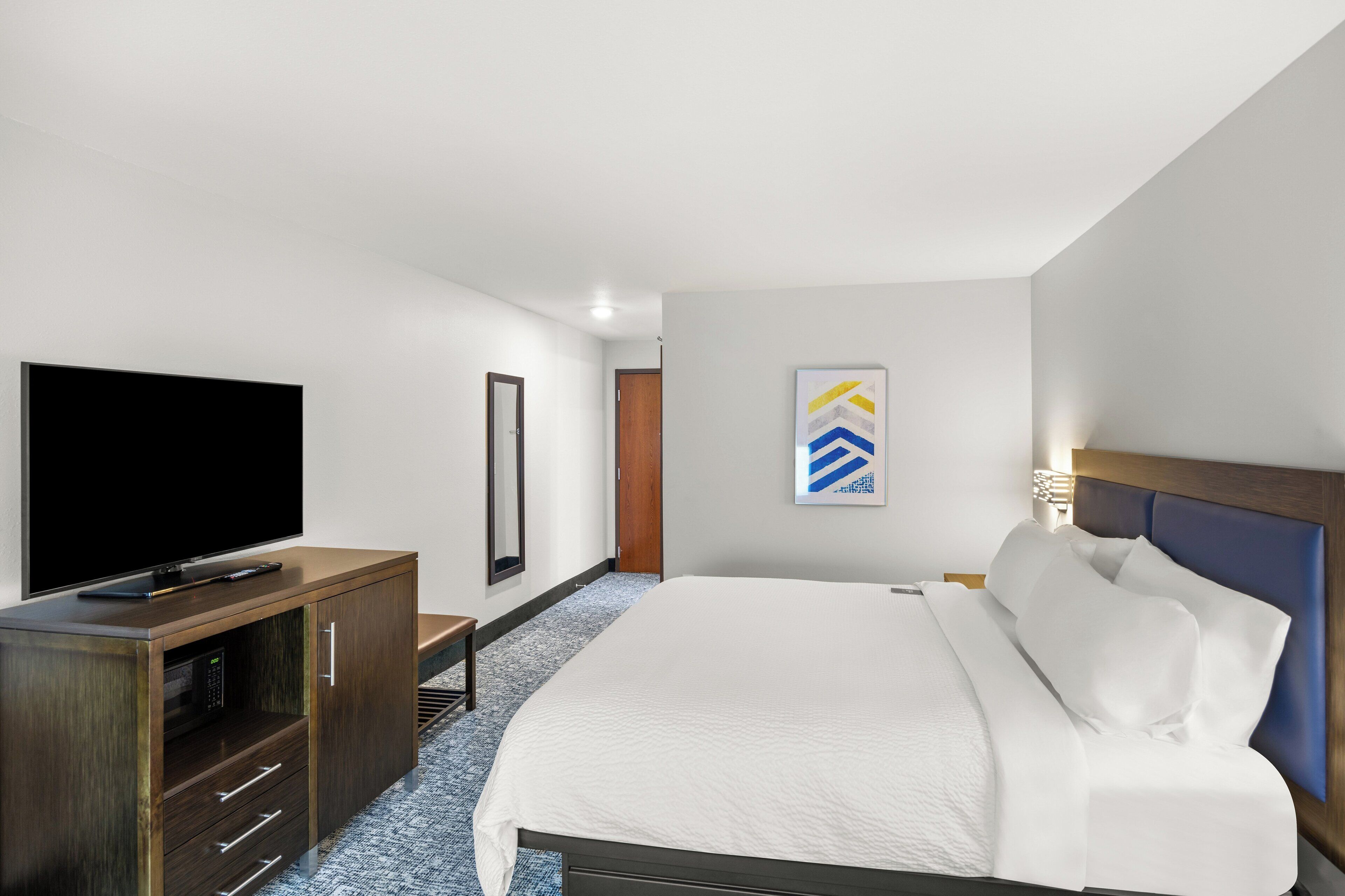 A modern hotel room with a large bed, a flat-screen TV, a wooden cabinet, and a framed artwork on the wall.