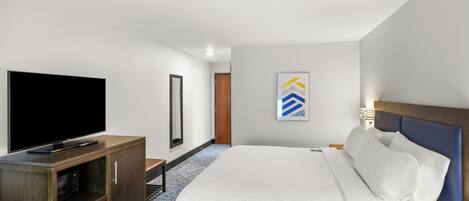 Un hotel moderno con una cama grande, un televisor de pantalla plana, un mueble de madera y una obra enmarcada en la pared.