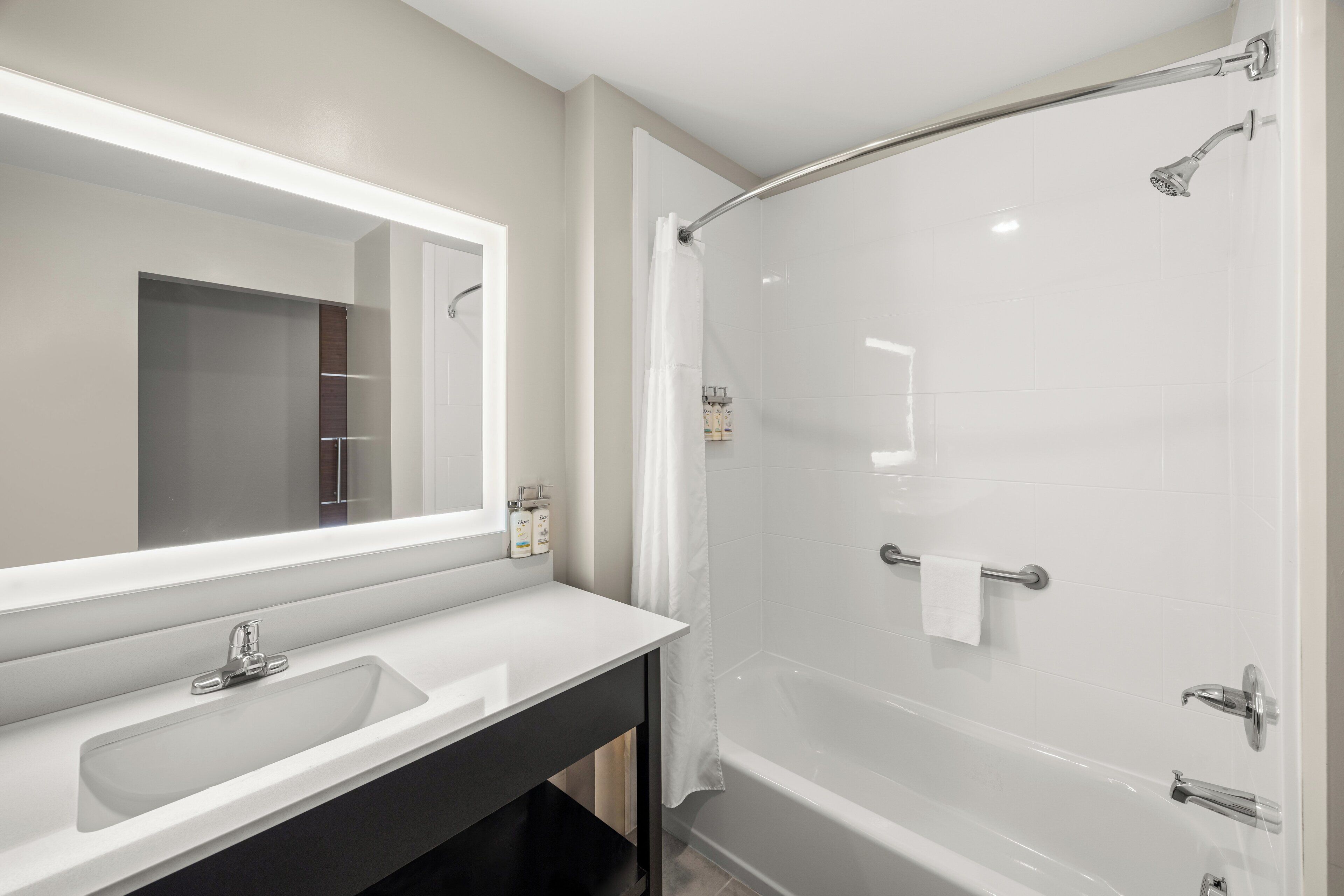 A modern bathroom with a large mirror, a sink, and a walk-in shower.