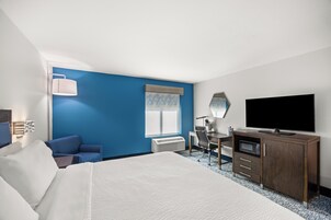 A hotel room with a large bed, a desk with a computer, a television, and a window with blinds.